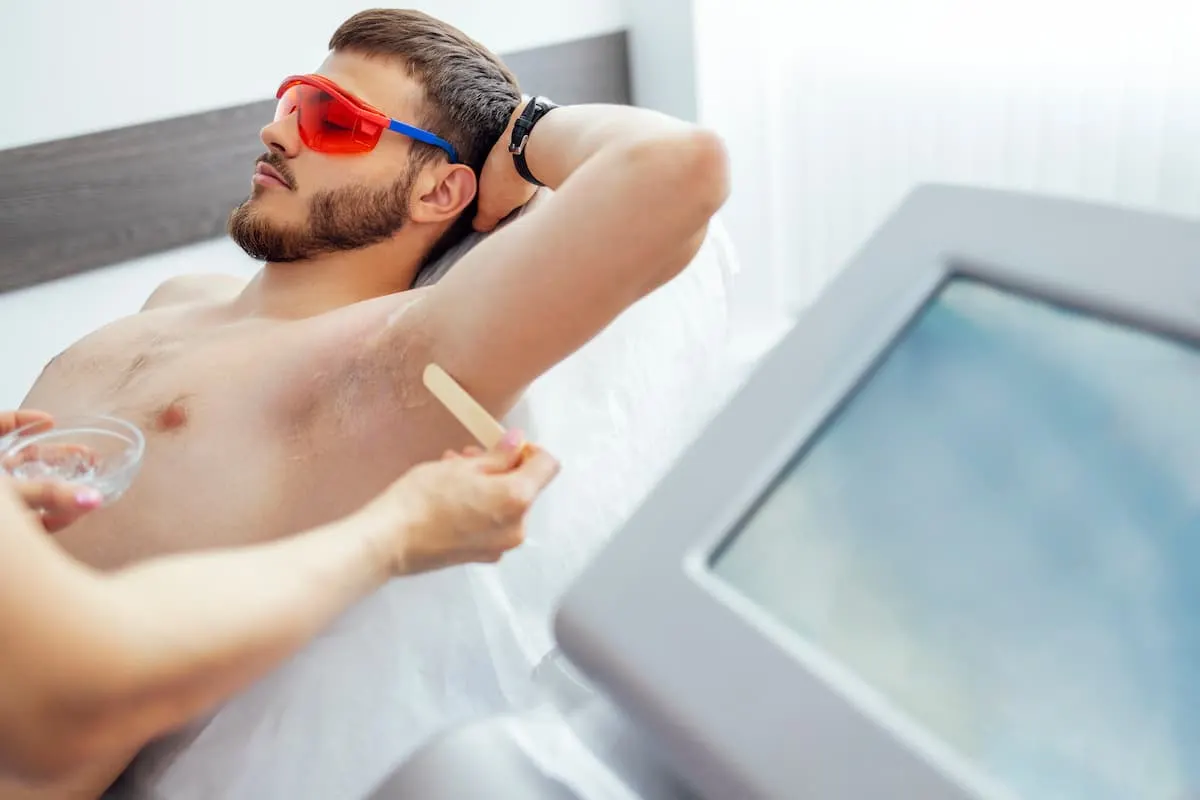 Hombre recibiendo tratamiento de depilación láser en la axila, recostado y con gafas de protección.