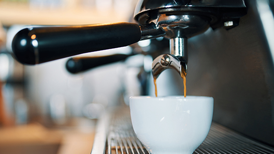 Kahve makinesinden beyaz bir fincana kahve akıyor. Makinenin sapı siyah renkte.