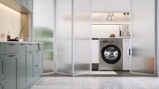 Aydınlık çamaşır odasında gri dolaplar, çamaşır makinesi ve buzlu cam bölmeler bulunur.