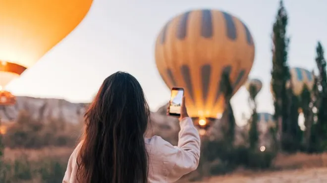 Kahverengi saçlı bir kadın, cep telefonuyla sıcak hava balonlarını fotoğraflıyor.