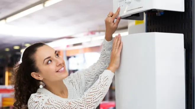 Gülümseyen kadın beyaz bir cihazın düğmesine basıyor, diğer eliyle cihazı destekliyor. Arka planda bulanık bir mağaza ortamı var.