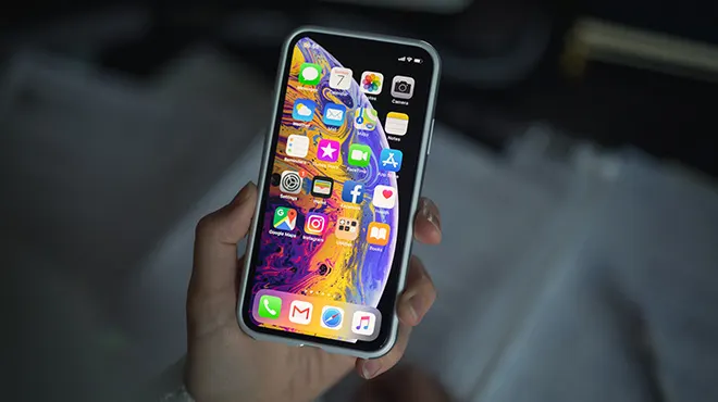 Bir el, ana ekranında renkli uygulama simgeleri olan bir akıllı telefonu tutuyor.