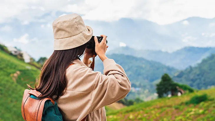 Dağlık alanda fotoğraf çeken bir kadın. Arka planda dağlar ve yeşillikler var.