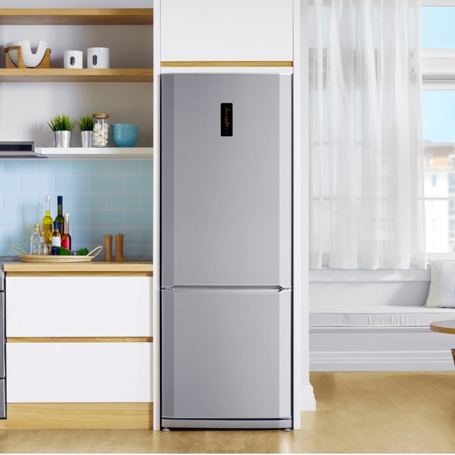 Mutfakta gri buzdolabı, beyaz dolaplar ve ahşap raflar. Pencereden ışık geliyor.