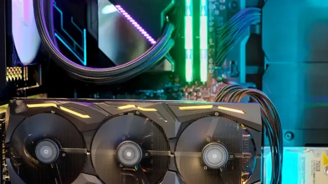 Yakın çekimde, renkli ışıklarla aydınlatılmış bilgisayar parçaları görülmektedir. Üç fanlı bir ekran kartı ve yeşil RAM çubukları dikkat çekmektedir.