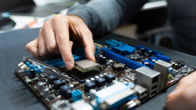 Bir kişinin anakart üzerine işlemci yerleştirdiği yakın çekim. Anakartta mavi ve siyah renkler hakim.