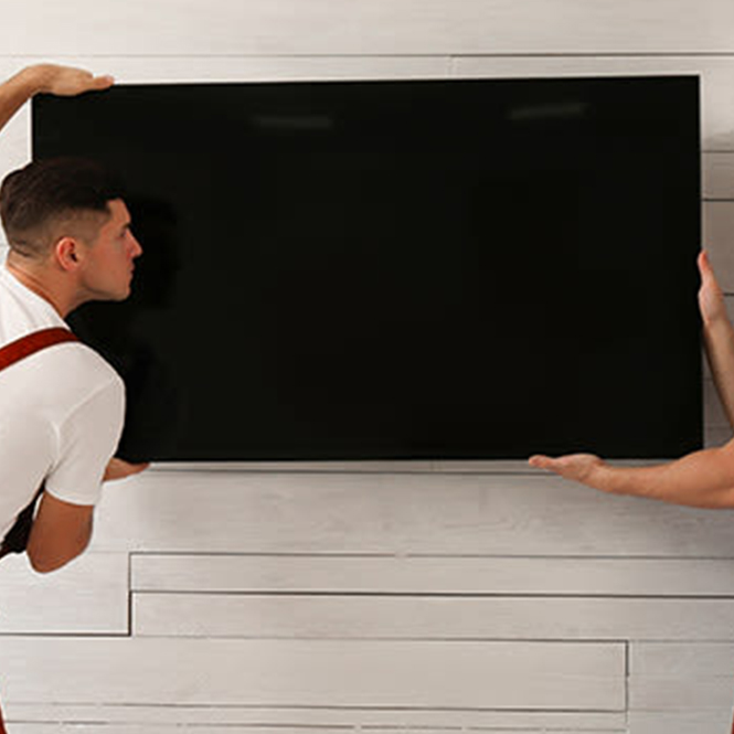 İki kişi beyaz duvar üzerine siyah bir televizyon yerleştiriyor. Bir kişi beyaz bir tişört giyiyor.