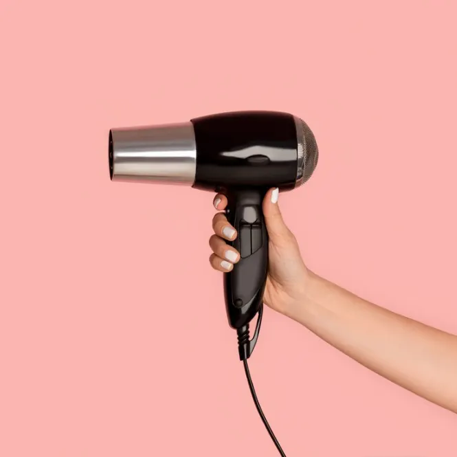 Pembe bir arka plan üzerinde siyah ve gümüş renkli bir saç kurutma makinesi tutan bir el.