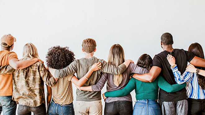 Bir grup insan, arkaları dönük, omuzları birbirine sarılmış, beyaz bir zemin önünde duruyor.