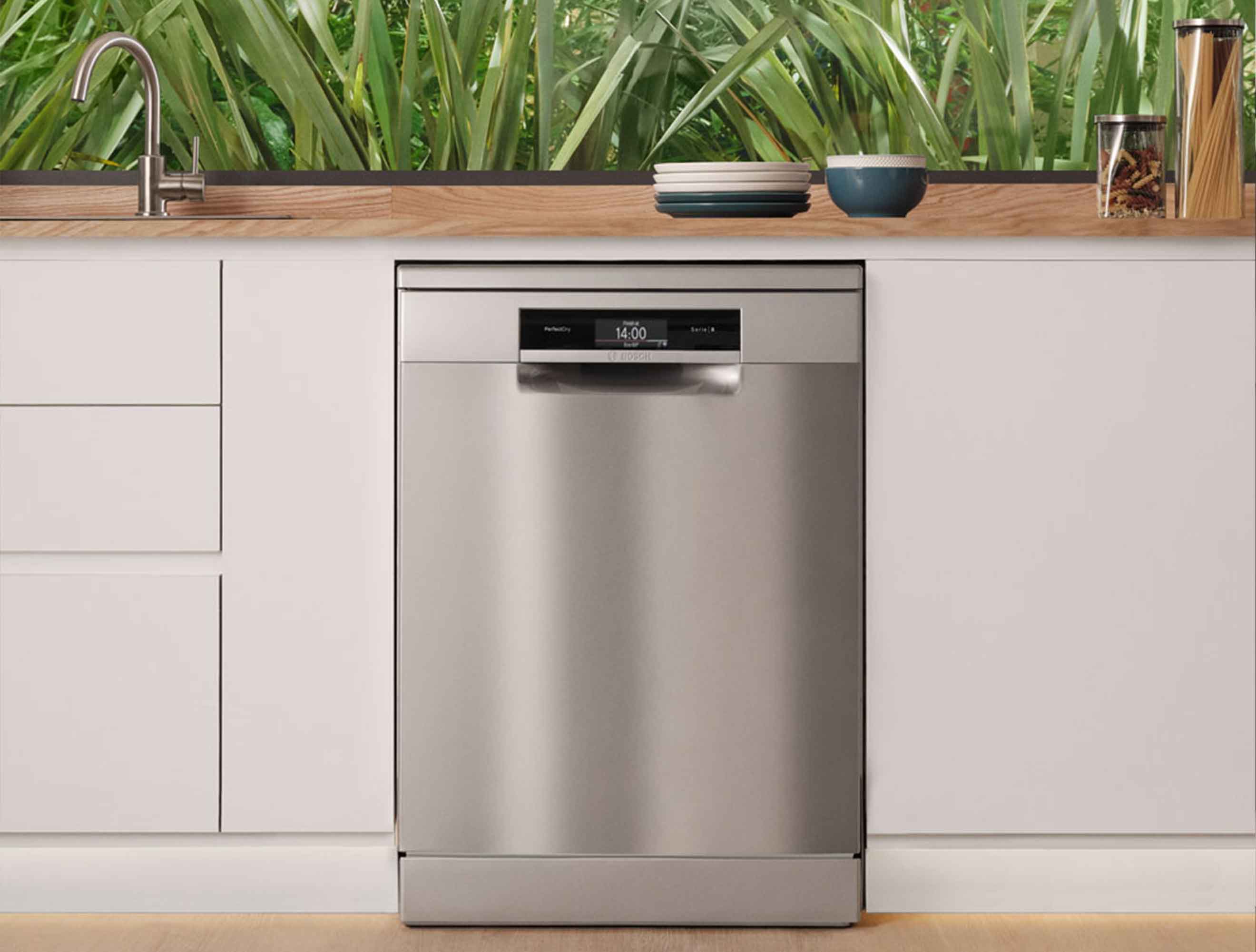 Gümüş bulaşık makinesi, beyaz dolaplı mutfakta. Tezgahta tabaklar, kase ve kavanozlarda makarna var.