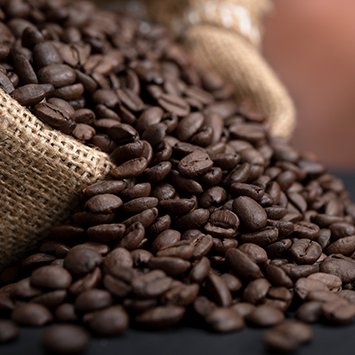 Jüt torbadan dökülen kahve çekirdekleri. Kahverengi tonları baskın, yakın çekim.