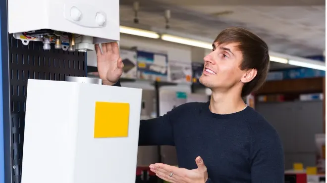 Bir adam beyaz eşyayı inceliyor. Cihazda sarı etiket var, arka planda raflar ve aydınlatma görülüyor.