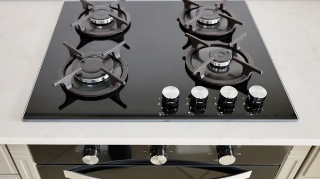 Siyah cam yüzeyli, dört gözlü ocak; her bir gözünde metal ızgaralar ve önünde kontrol düğmeleri bulunur. Tezgah beyaz renktedir.