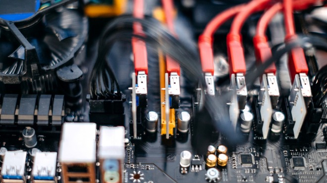 Yakın çekimde anakart ve kırmızı kabloların detayları, elektronik bileşenler görülüyor.