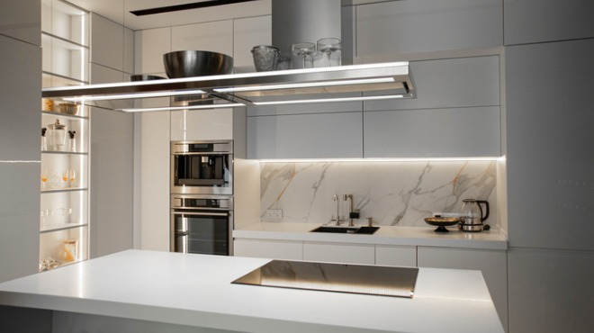 Aydınlık, modern mutfak; beyaz dolaplar, paslanmaz çelik cihazlar, mermer desenli duvar ve ada tezgahı içerir.