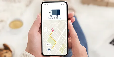 Bir kişi, ekranda harita ve teslimat kamyonu olan bir akıllı telefonu tutuyor. Harita, pembe bir işaretçi ve sarı bir rotaya sahip.