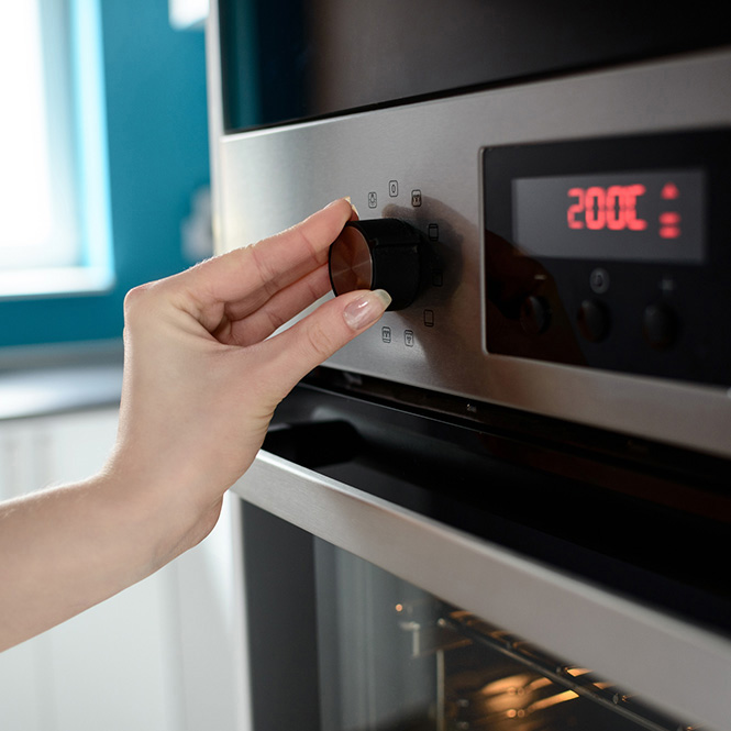 Önden görünümde, gri bir çamaşır makinesi bulunmaktadır. Makinenin önünde yuvarlak, siyah bir kapak ve üstünde dijital bir ekran mevcuttur.