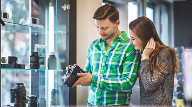 Bir adam ve bir kadın, vitrinde sergilenen kameralara bakıyorlar. Adam bir kamera tutuyor.