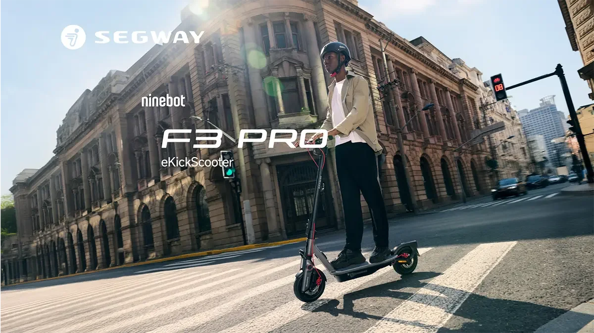 Şehirde Ninebot F3 Pro eKickScooter'ı kullanan kasklı bir adam. Arka planda binalar ve trafik ışıkları var.