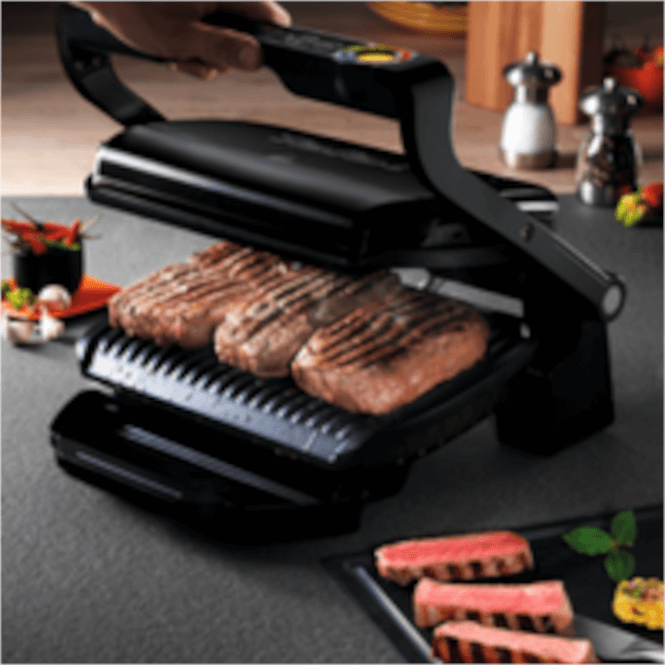 Siyah ızgarada pişmiş etler var. Masada baharatlıklar ve tabakta et dilimleri görülüyor.