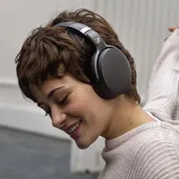 Kahverengi saçlı, kulaklıklı kadın yana bakıyor, beyaz bir kazak giyiyor. Arka planda beyaz duvar var.