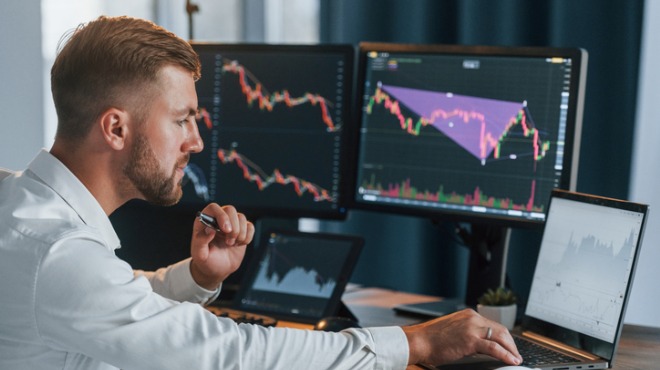 Sakal, sakallı bir adam bilgisayar ekranlarına bakıyor. Ekranda grafikler ve tablolar görülüyor.