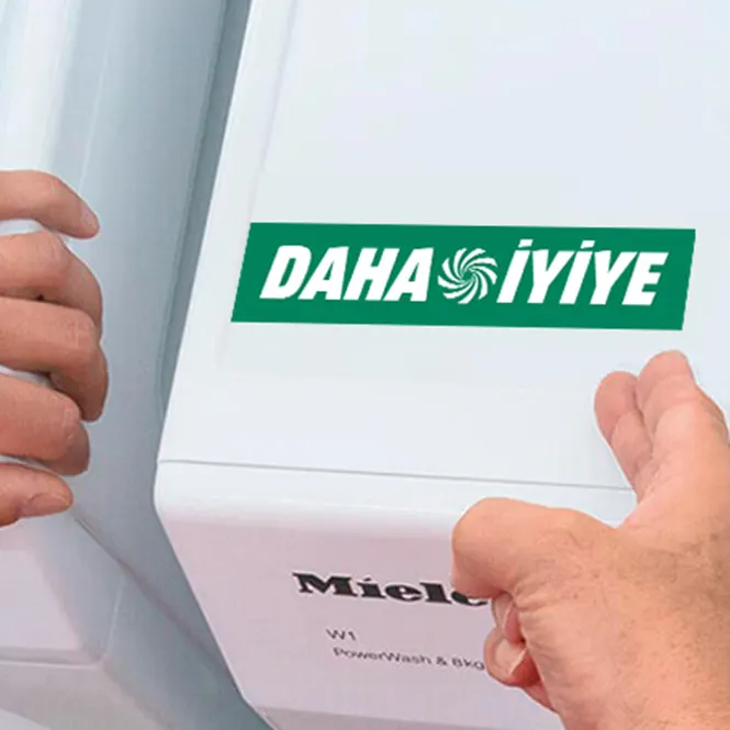 Beyaz Miele çamaşır makinesi üzerinde "DAHA İYİYE" yazısı ve iki el bulunuyor.