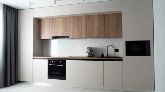 Açık renk dolaplı, ahşap detaylı, modern mutfak. Siyah fırın ve evye mevcut. Perde sol tarafta.