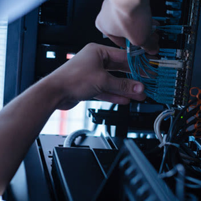 Bir kişi sunucu kablosundaki mavi kabloları düzenliyor. Kablolar ve donanım yoğun bir şekilde paketlenmiş.