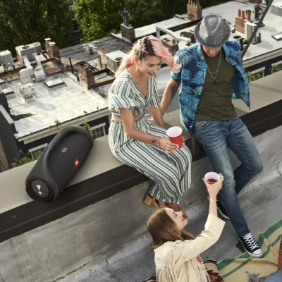 Çatıdaki üç kişi, bardak tutuyor. Hoparlör ve şehir manzarası arka planda.