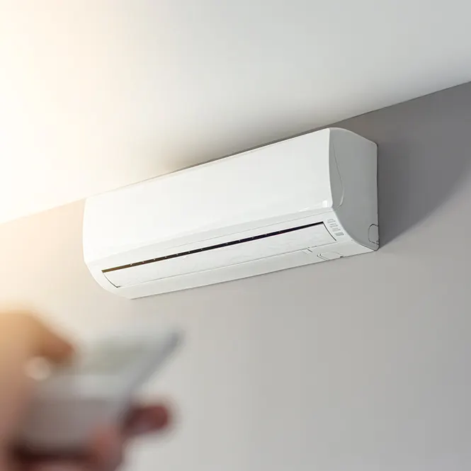 Duvara monte beyaz klima ünitesi, uzaktan kumanda tutan bir el.