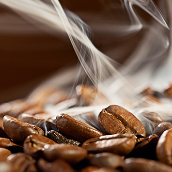 Kahverengi kahve çekirdekleri yığını ve buharlı kahve dumanı, kahve deneyimini canlandırıyor.