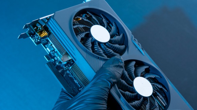 Mavi eldivenli bir el, iki beyaz merkezli fanı olan mavi bir ekran kartı tutuyor.