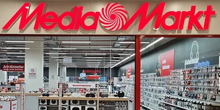 Mediamarkt mağazasının dış cephesi. Kırmızı logolu tabela ve mağaza içi ürün rafları görünüyor.