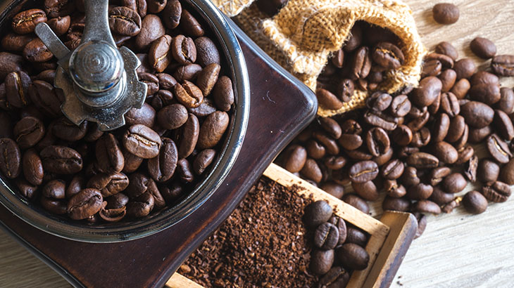 Kahve çekirdekleri, öğütücü ve çekilmiş kahve içeren bir görüntü. Çekirdekler ve çekilmiş kahve açık kahverengidir.