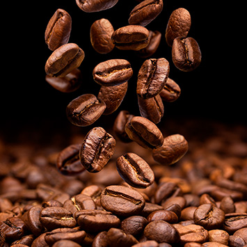 Siyah fonda kahverengi kahve çekirdekleri düşüyor. Yığın halinde kahve çekirdekleri görülüyor.