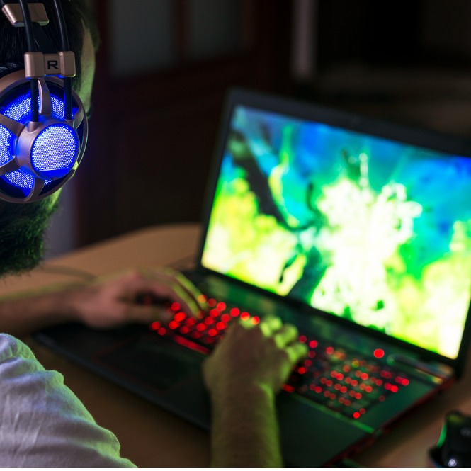 Kulaklıklı, sakallı bir kişi, kırmızı ışıklı klavyede yazı yazarken dizüstü bilgisayar kullanıyor.