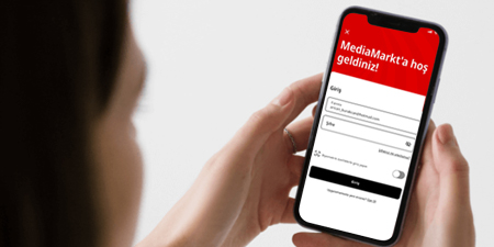 Bir kişi, MediaMarkt uygulamasının açık olduğu bir akıllı telefon tutuyor. Ekran kırmızı ve beyaz renkte.