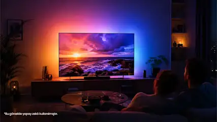 Evin salonunda Ambilight TV bulunuyor ve karşısında oturup televizyon izleyen bir kadın ve bir adam