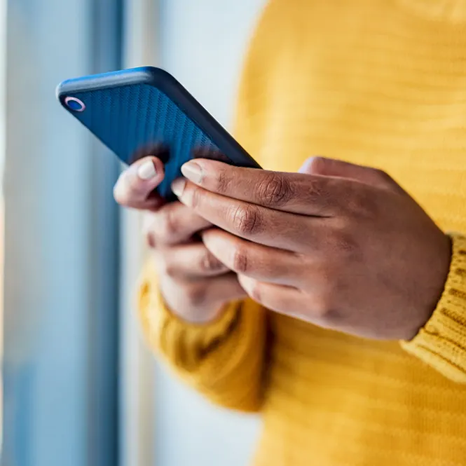 Sarı kazaklı bir kişi, mavi kasalı bir akıllı telefonu tutuyor. Arka planda mavi perdeler var.