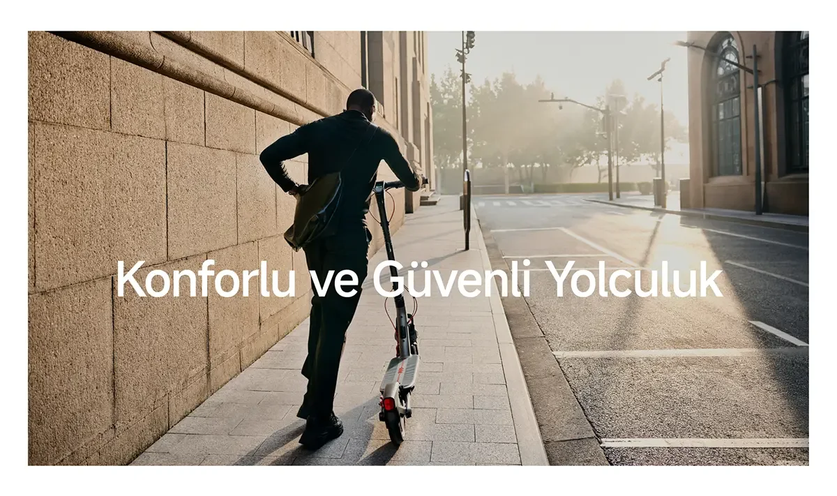 Şehirde, elektrikli scooter süren, çantalı bir adam. Arka planda binalar ve yol var.