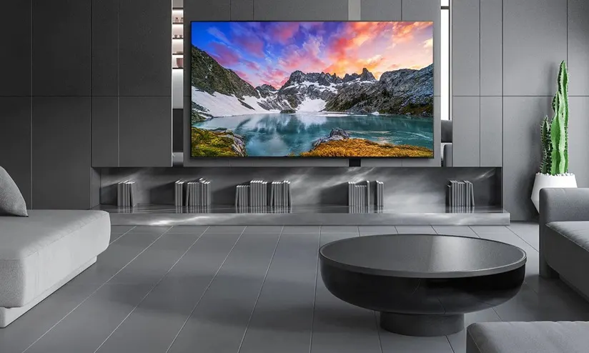 Geniş ekran TV'nin altında kitaplar olan, gri tonlamalı modern bir oturma odası görülmektedir.