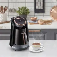 Siyah Türk kahvesi makinesi yanında kahve fincanı. Arka planda mutfak tezgahı ve aksesuarlar görülüyor.