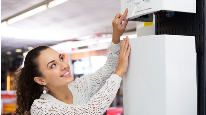 Gülümseyen kadın, beyaz bir eşyaya dokunuyor. Açık renkli bir bluz giyiyor ve saçları toplanmış.