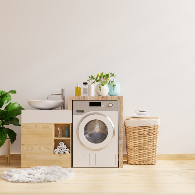 Açık renkli odada çamaşır makinesi, lavabo, hasır sepet ve bitki bulunuyor.