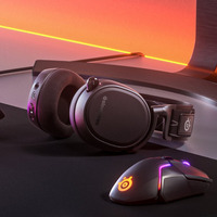 Siyah kulaklık ve fare, turuncu ışık efektli oyun masası üzerinde duruyor.