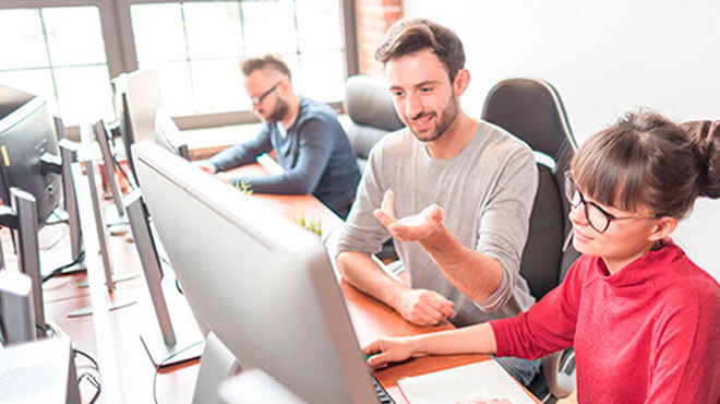 Ofiste bilgisayarlar başında çalışan insanlar. Ön planda kırmızı giyen kadın ve gri giyen erkek var.