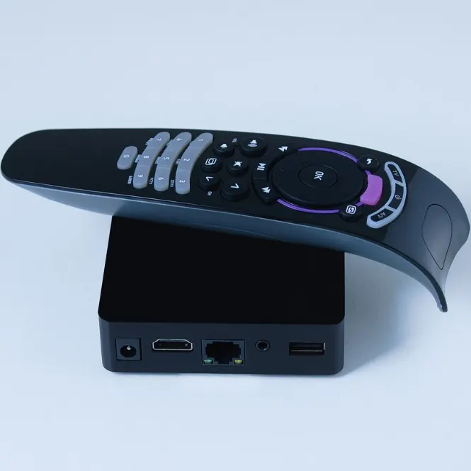 Siyah bir kutunun üzerinde, uzaktan kumanda cihazı duruyor. Kumandanın üzerinde düğmeler ve mor detaylar bulunuyor.