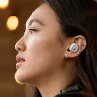 Bir kadının kulaklığının yakın çekim fotoğrafı. Kadın, kahverengi saçlı ve bej tenli. Arka plan bulanık.