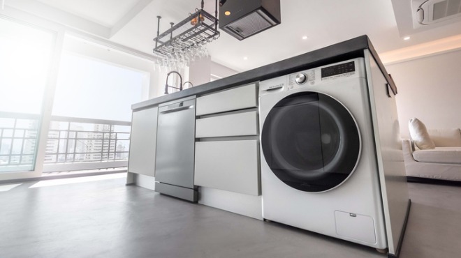 Aydınlık mutfakta bulaşık makinesi, çekmeceler ve çamaşır makinesi olan ada tezgahı görülüyor.